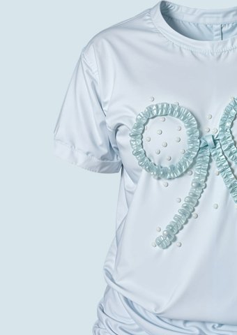 Primer plano de una remera azul pastel con lazo texturizado en relieve, detalle de manga y textura suave.